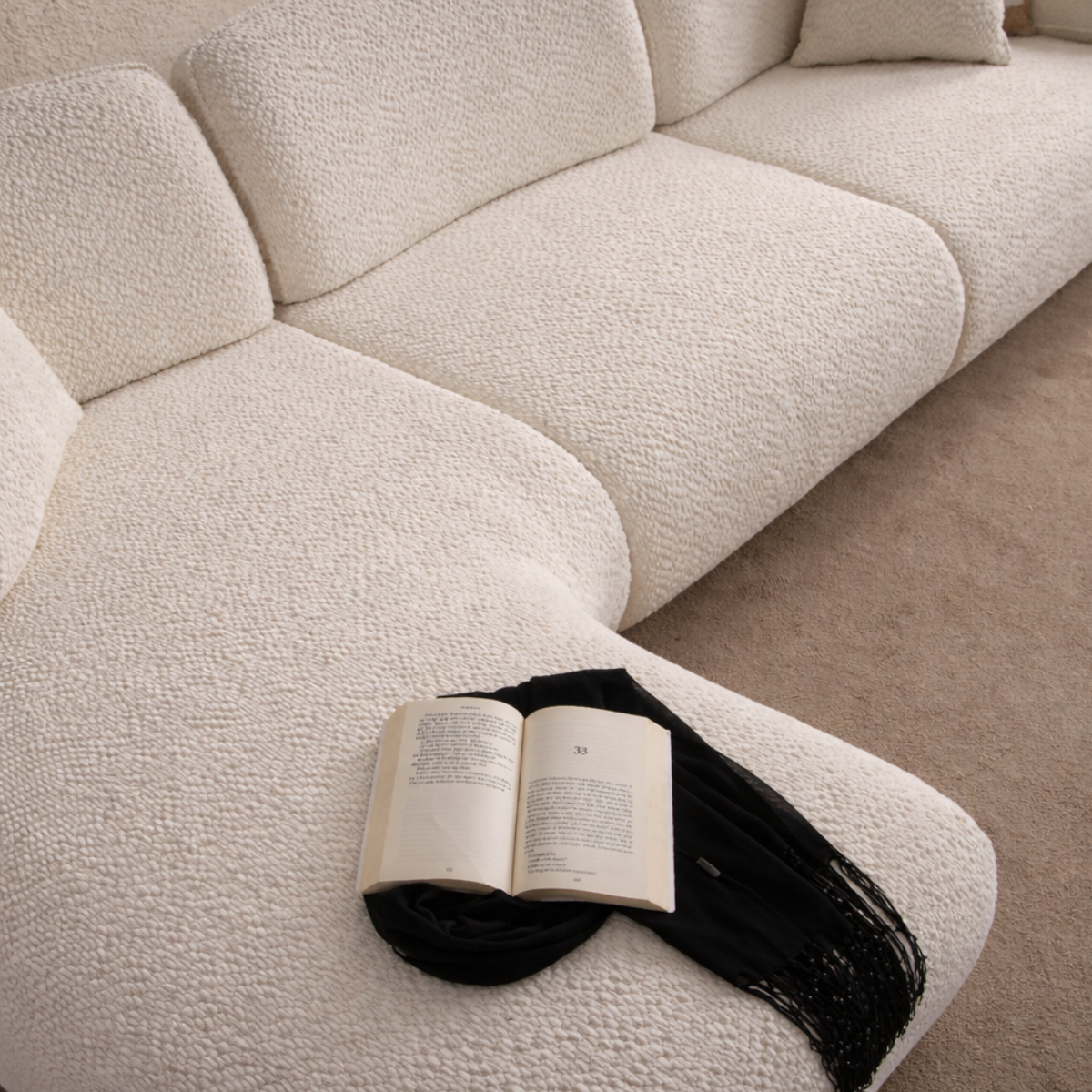 Open book on a textured beige sofa with a black cat lying next to it.