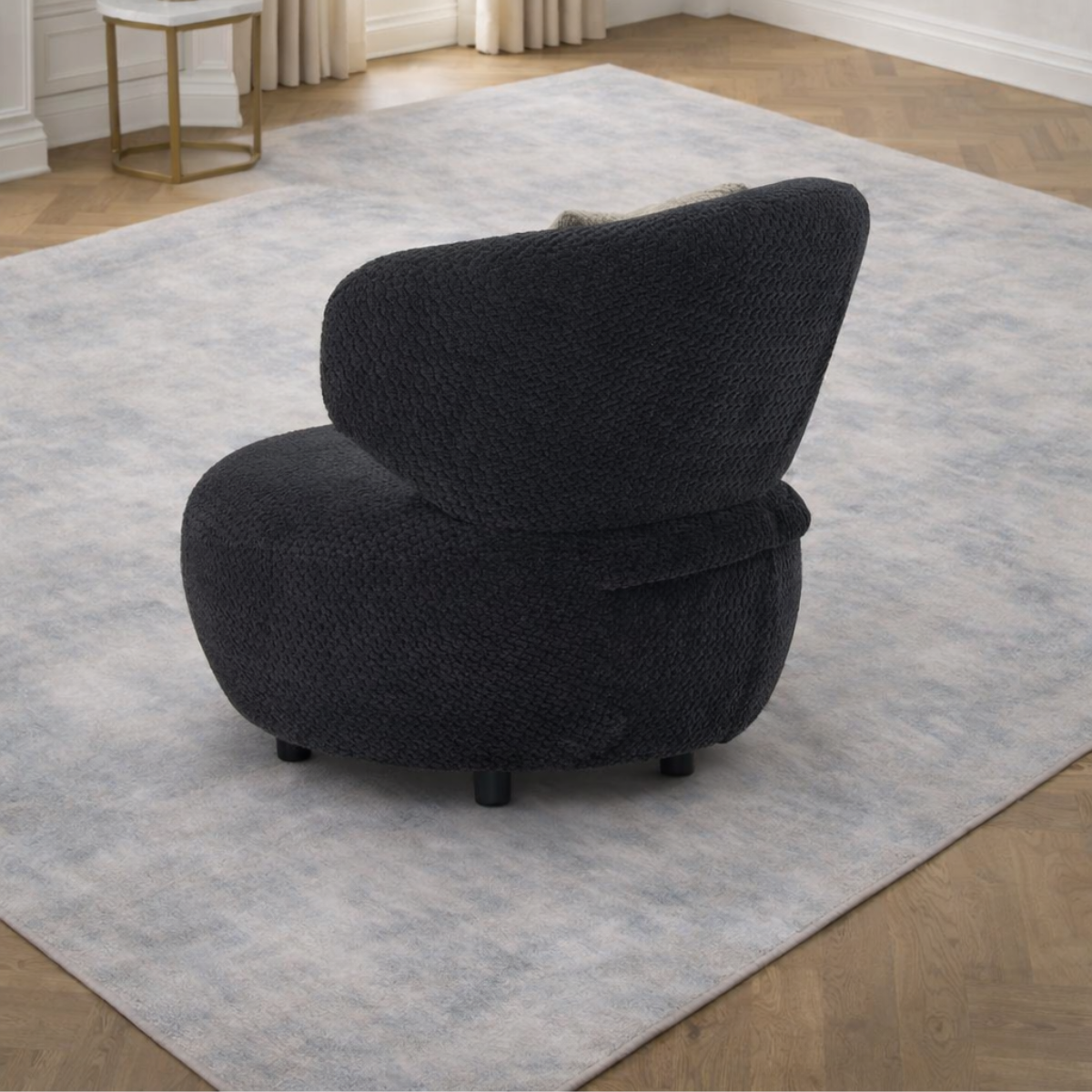 Black textured armchair on a light gray rug in a room with wooden flooring.