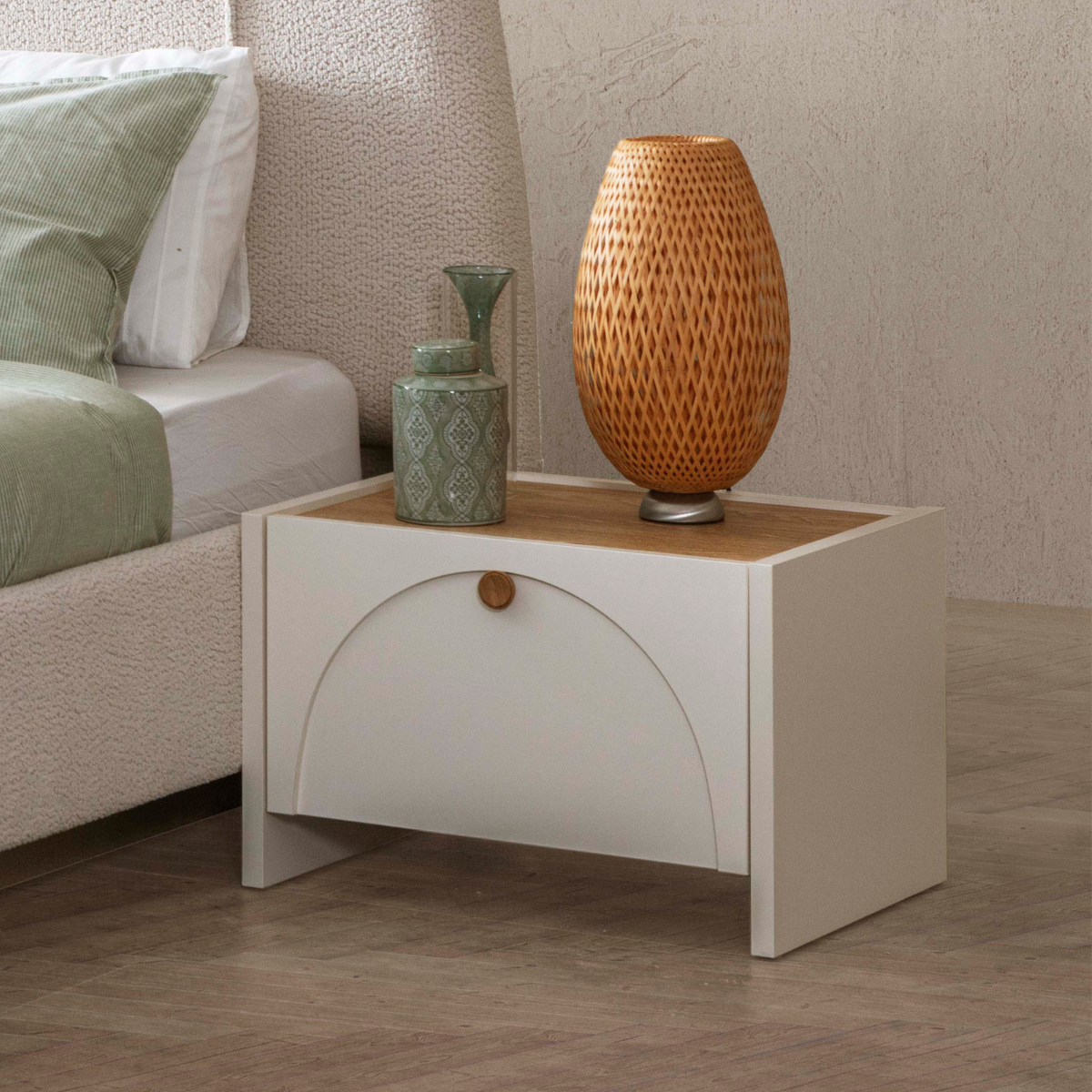 White nightstand with wooden top holding a decorative lamp and vase, next to a bed with green and white bedding.