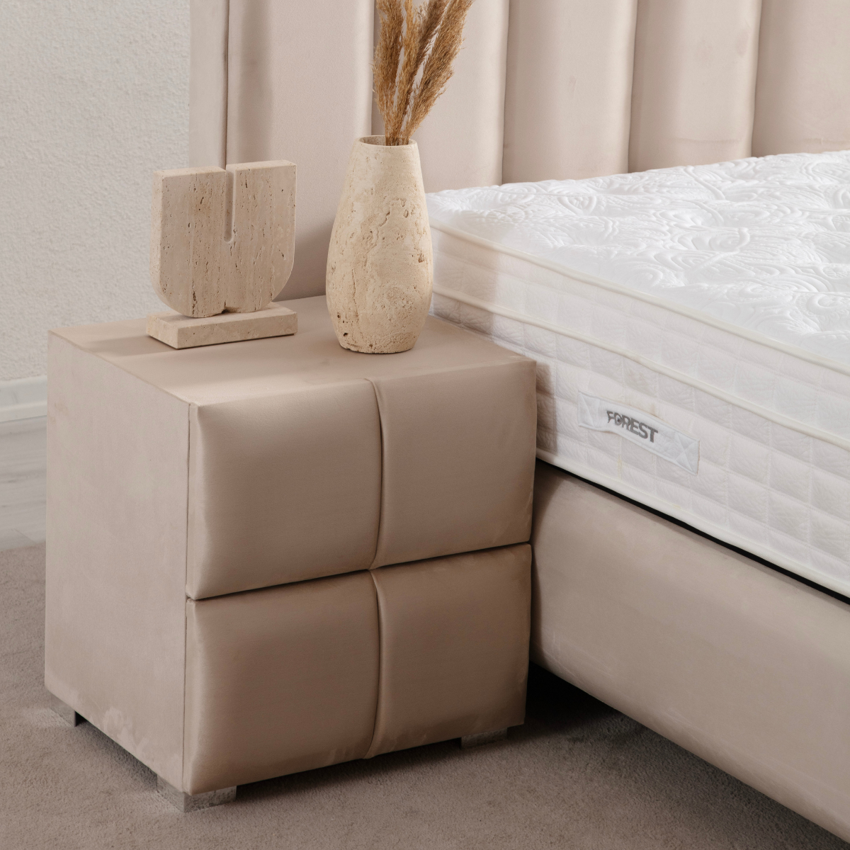 Beige nightstand next to a bed with a mattress, featuring decorative items on top.